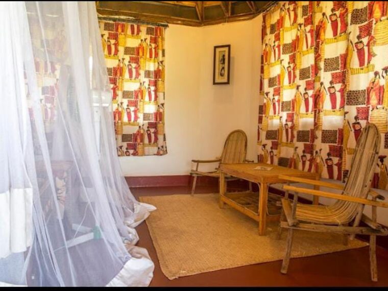 A sitting area with cane chairs and a bed under a mosquito net